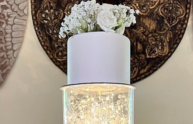 Bolo de casamento branco com rosas e gipsófila no topo e um andar iluminado por luzes